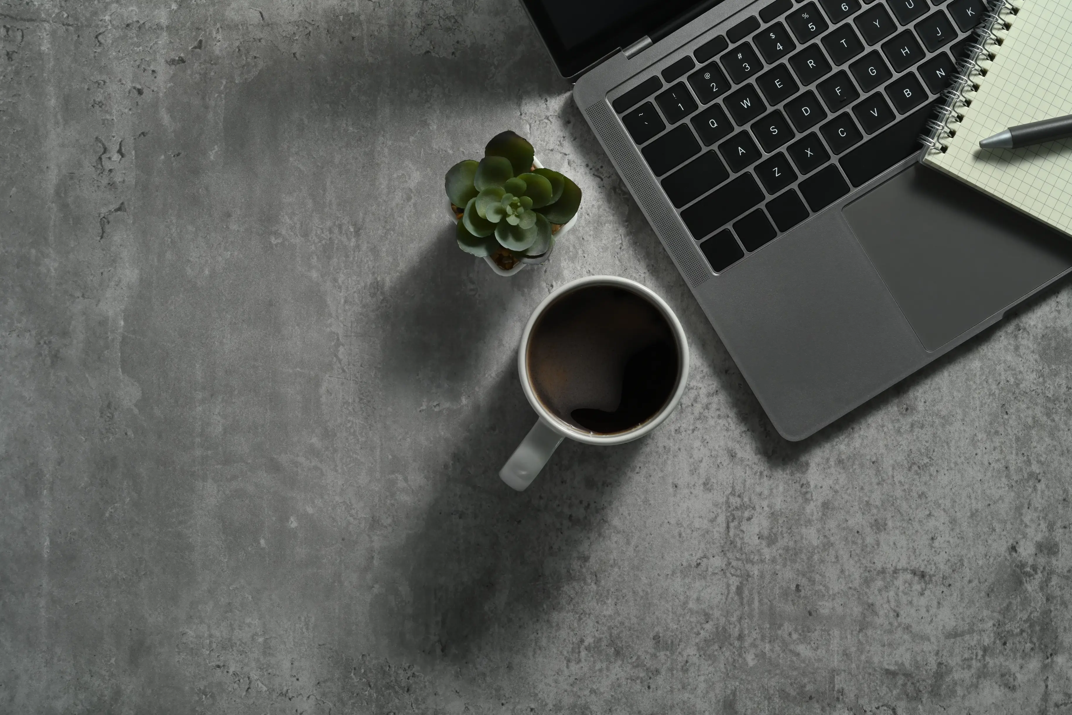Laptop with coffee and notebook on a concrete office desk