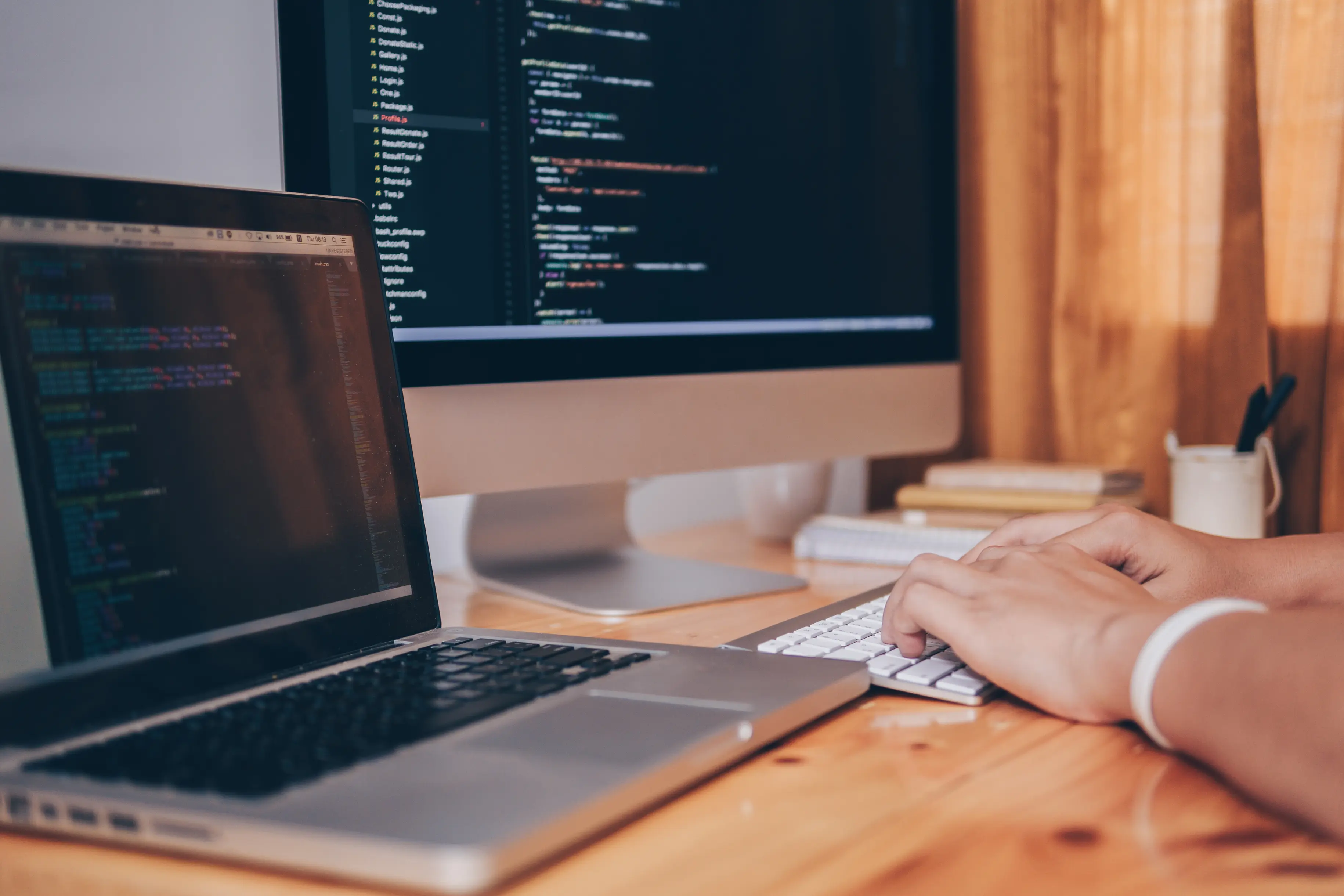 Hands typing code on a laptop at a desktop