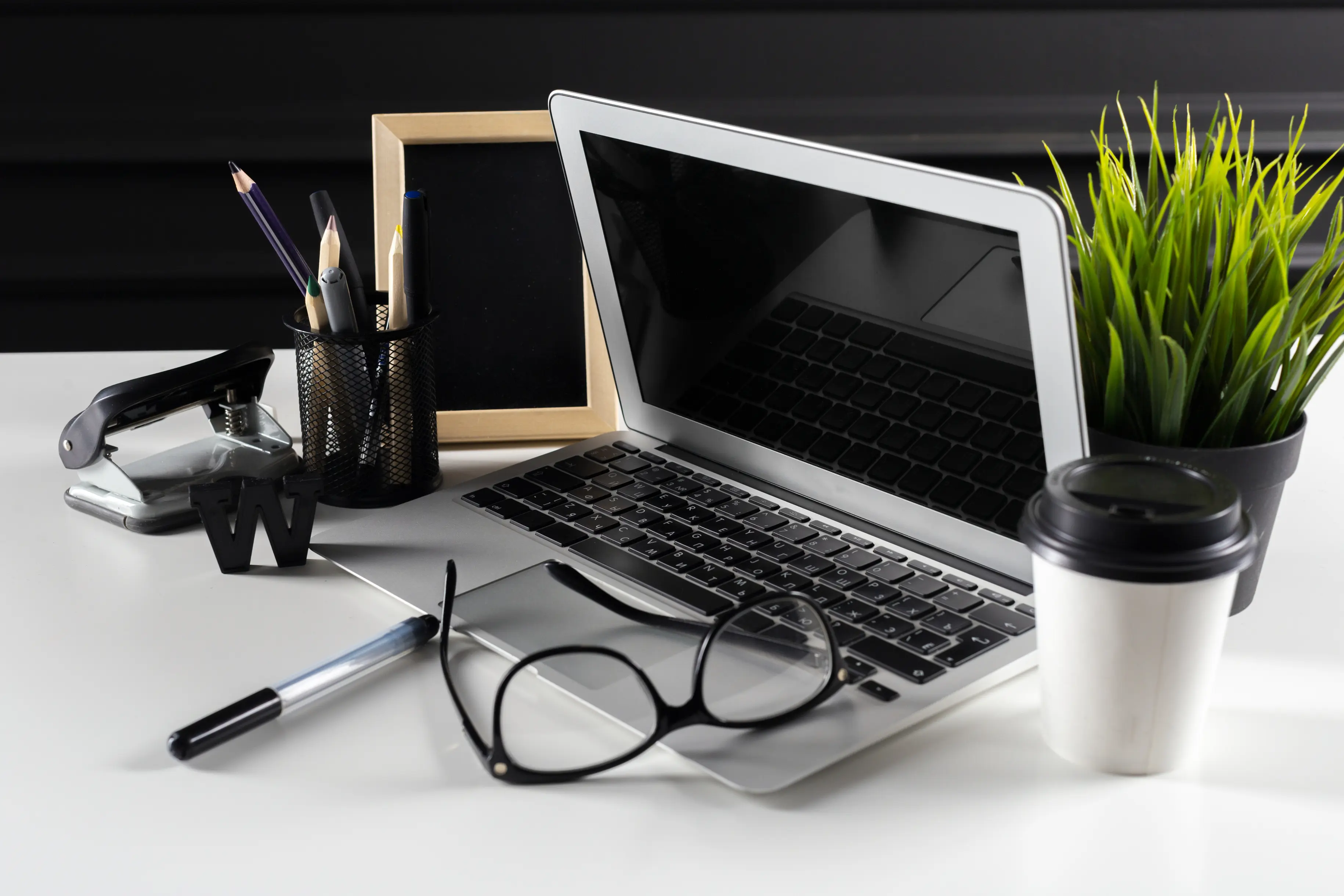 Laptop with glasses, plant, pens and coffee, angled view