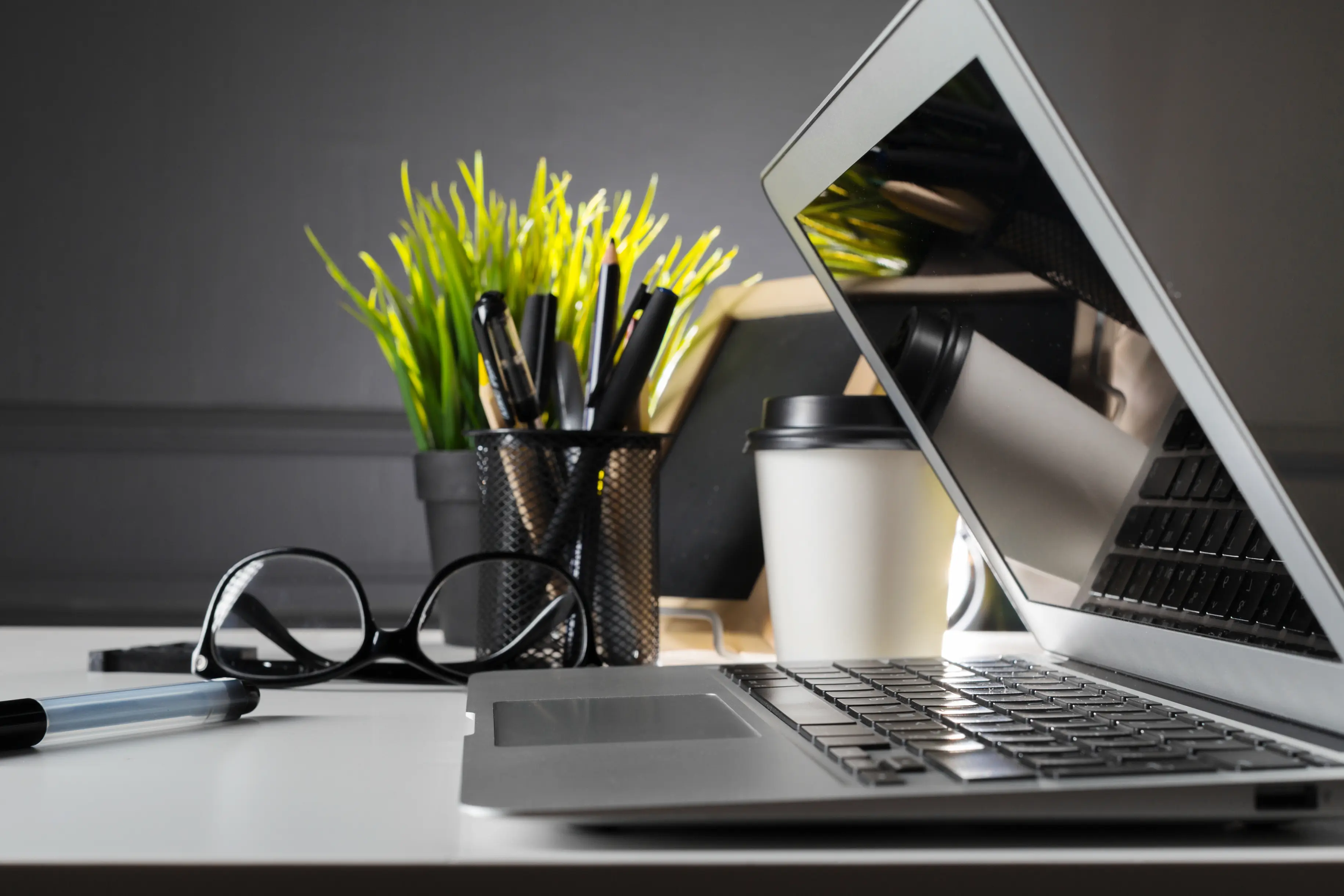 Laptop with glasses, plant, pens and coffee seen from the side