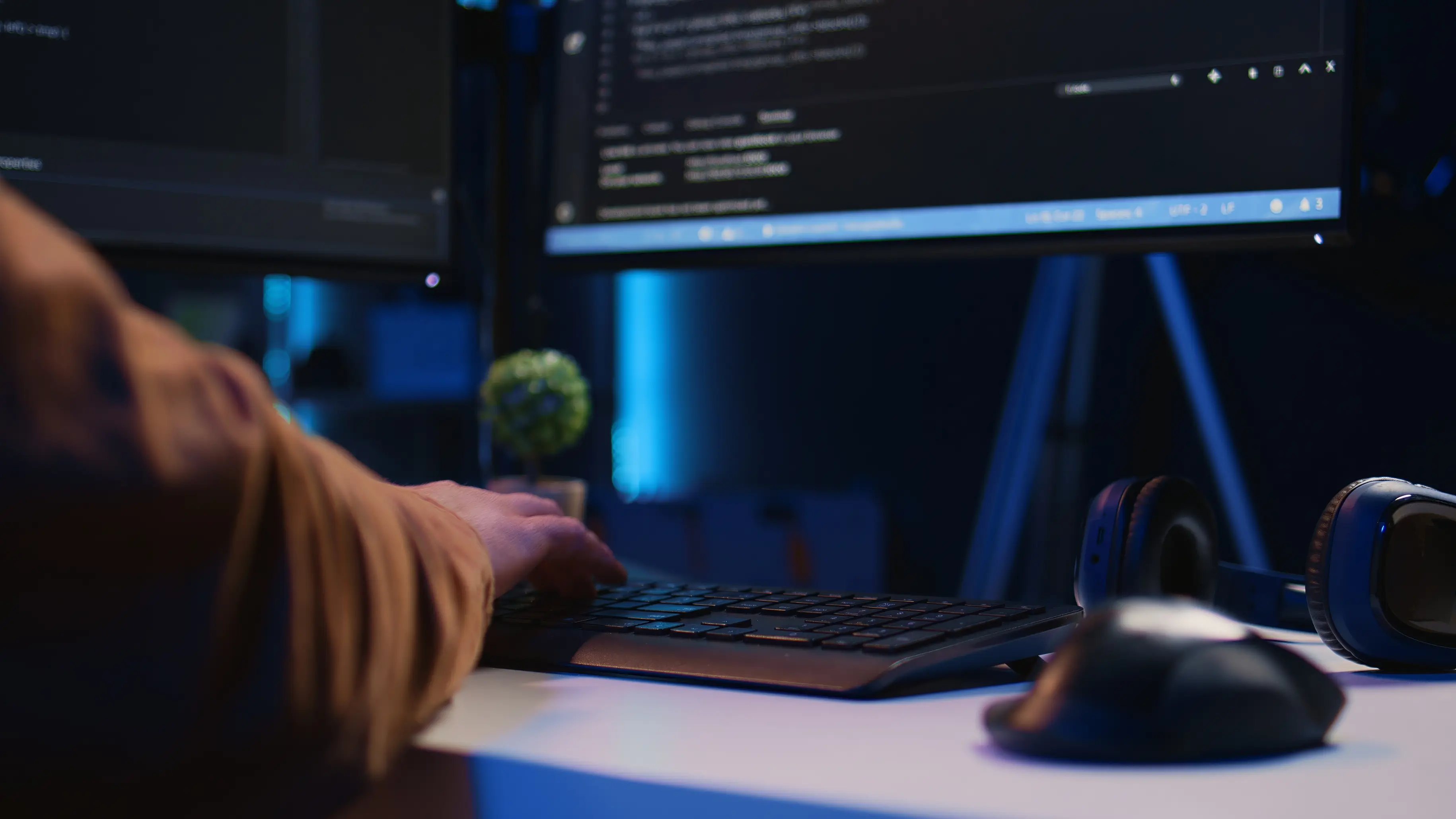 Person typing code close-up with headphones and a plant