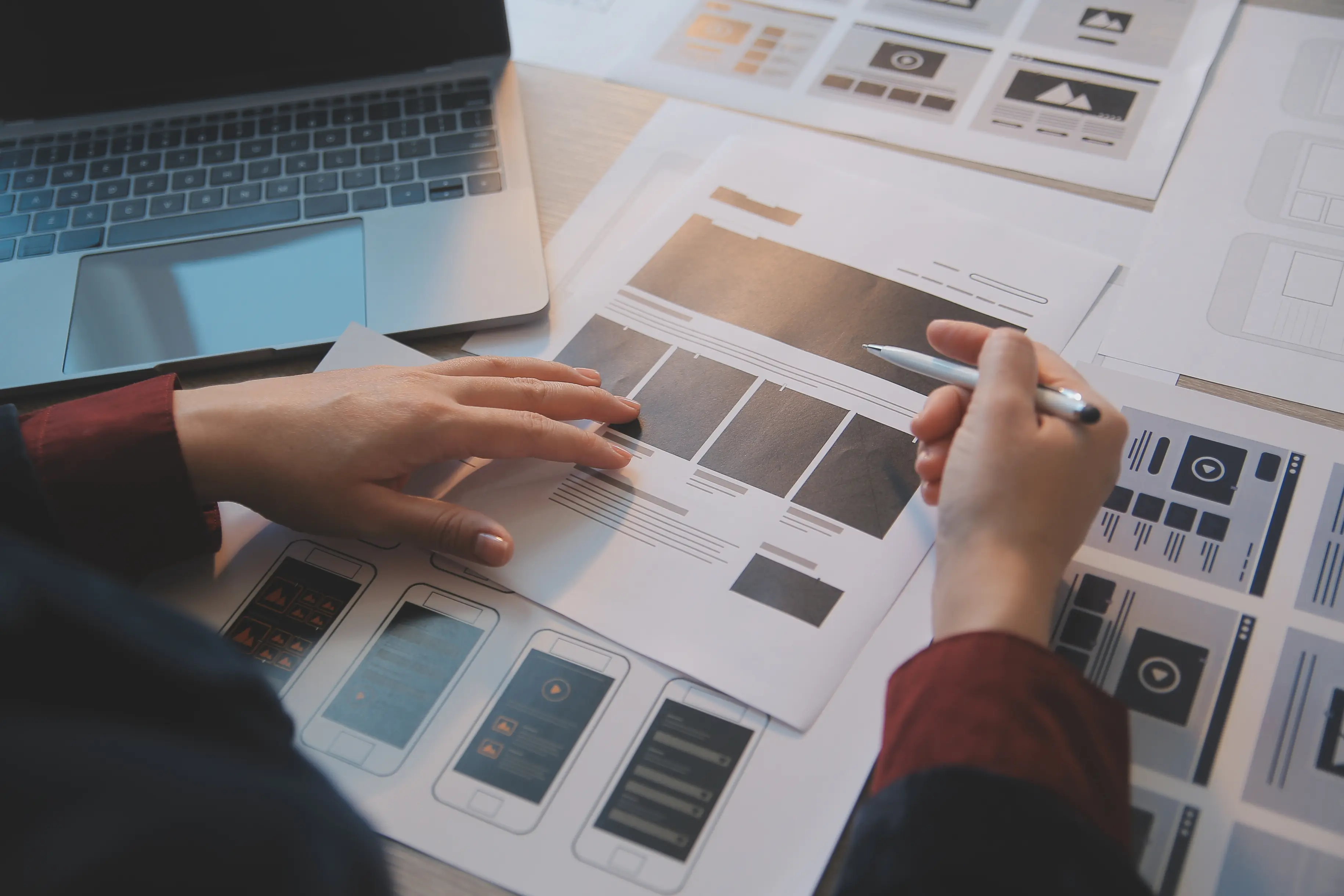 Person pointing at phone and desktop UI/UX design on a laptop