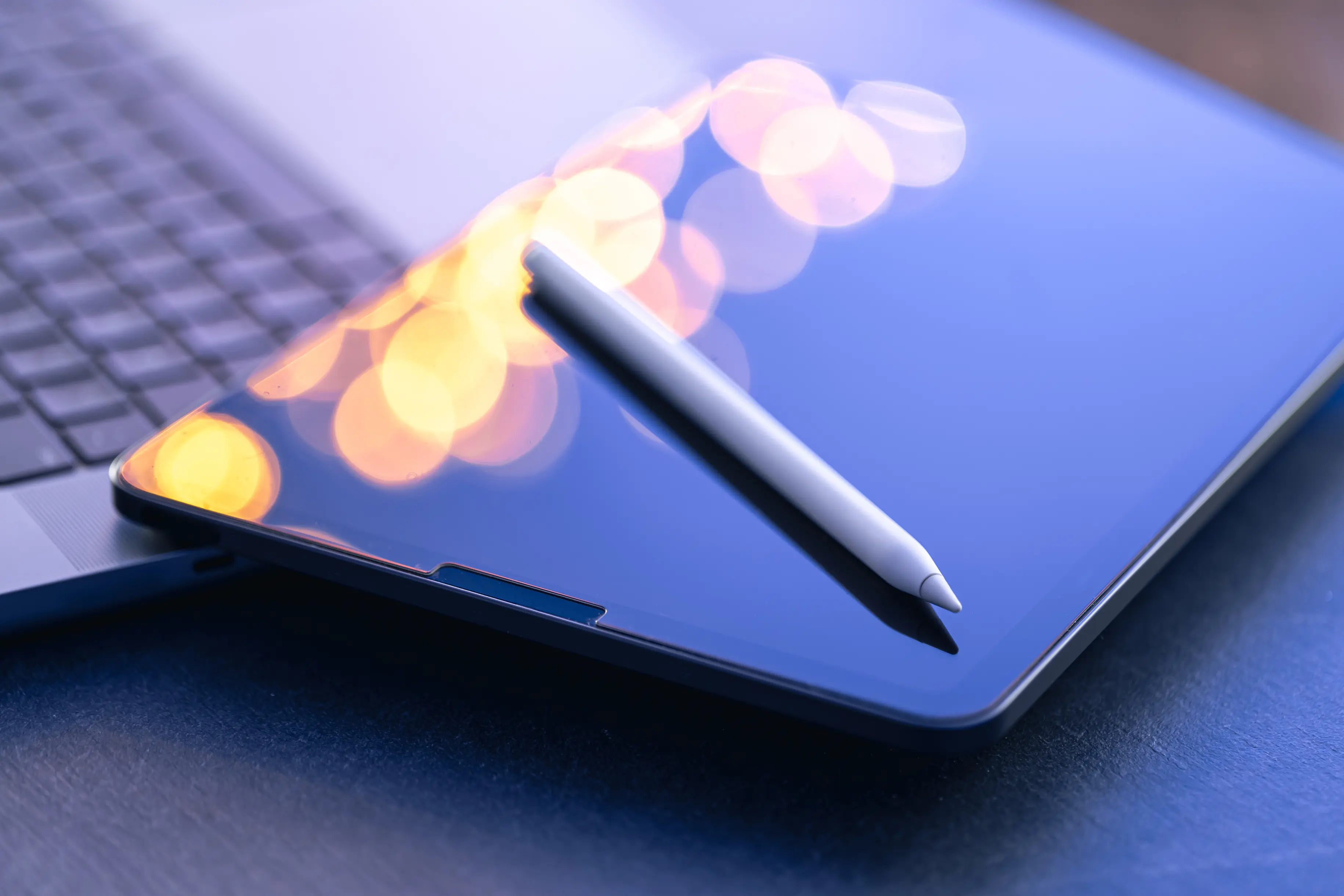 Close-up of a tablet and stylus next to a laptop